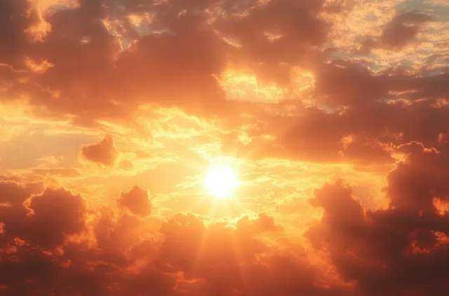 Sunburst shines through dense orange and yellow clouds, creating a warm glowing sunset sky.