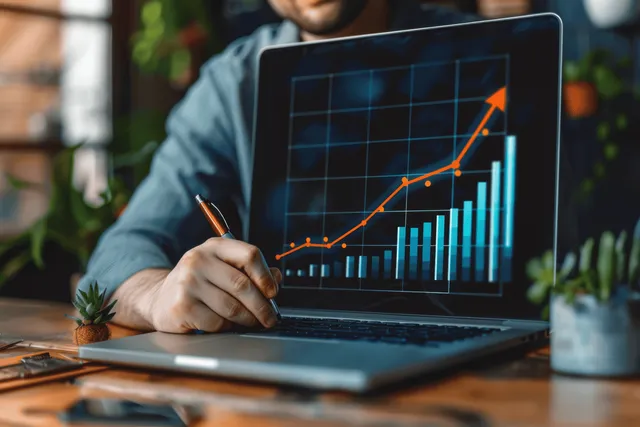 Person’s hand writes notes beside a laptop showing an upward growth chart with highlighted targets.