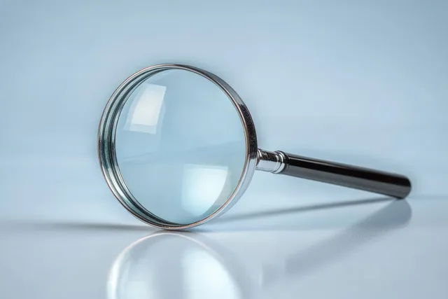 Handheld magnifying glass with a black handle reflecting light on a smooth blue surface.