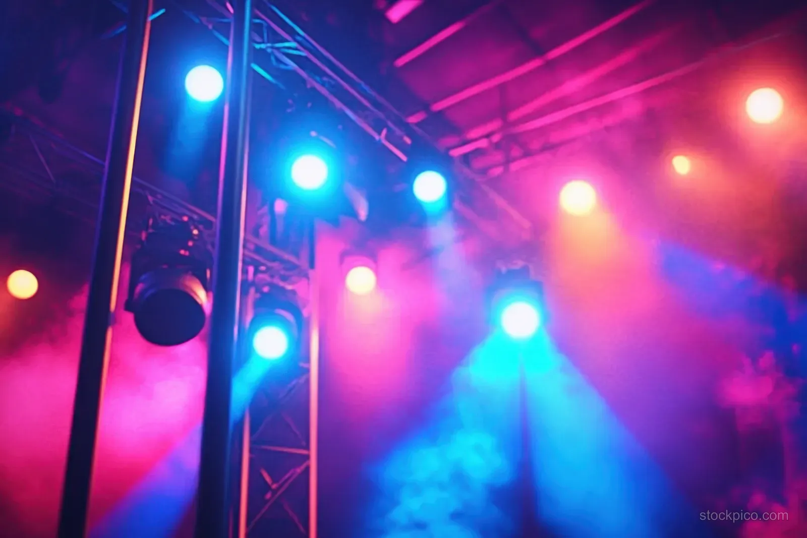 Colorful spotlights beam through stage trusses and light smoke in a nighttime concert setting.