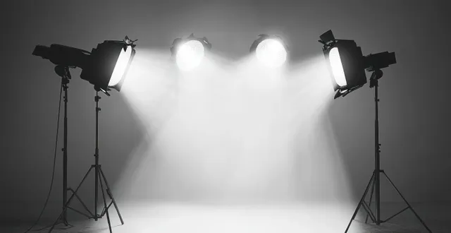 Four studio spotlights on stands casting focused light beams on empty gray backdrop