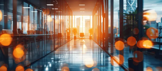 Panoramic office corridor with glass walls and warm reflections, with blurred city lights in the background.