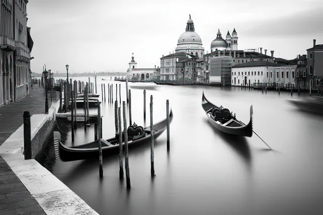 Gondolas rest beside wooden posts in a quiet Venetian canal with domed buildings under cloudy skies.