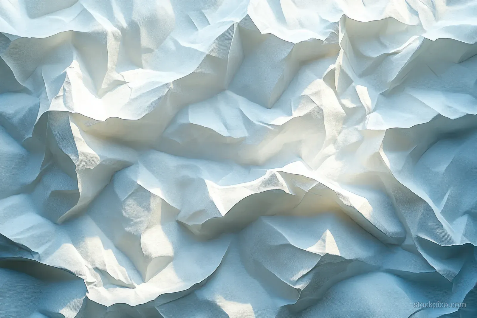 Crumpled white paper fills the frame with soft natural light, layered folds, and visible creased shadows.