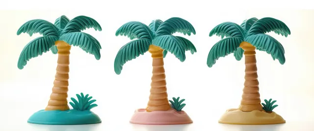 Three miniature plastic palm trees on colorful bases against a clean white background