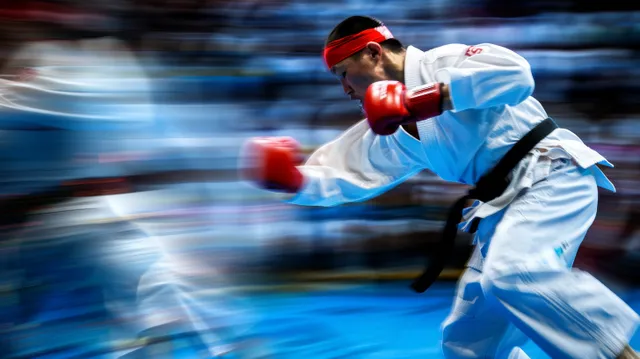 A male karateka in red gloves and a white gi throws a fast strike with motion blur.