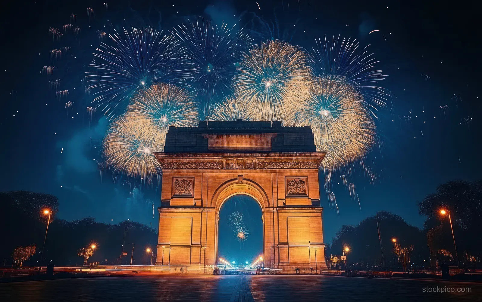 Golden fireworks burst behind a brightly lit historic arch monument at night over an empty city street.