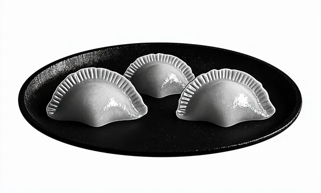 Three uncooked dumplings with pleated edges arranged on a black plate against a white background.