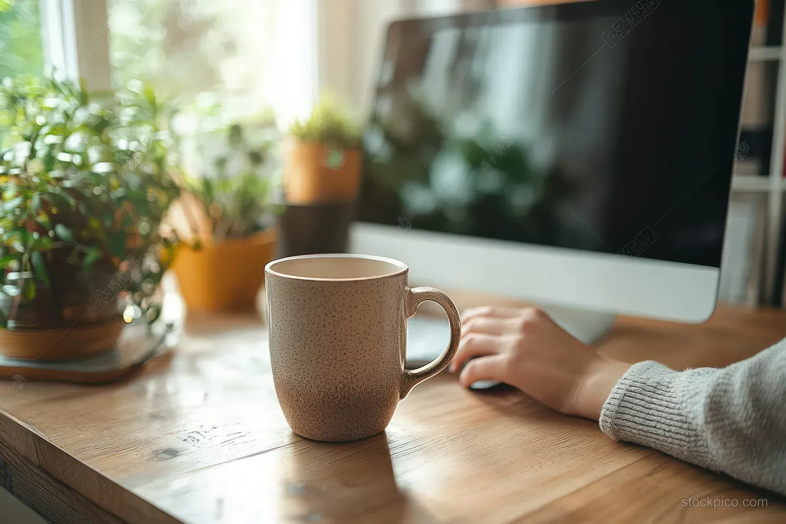 A coffee mug and a laptop rest on a minimalist desk while hands type at home office.