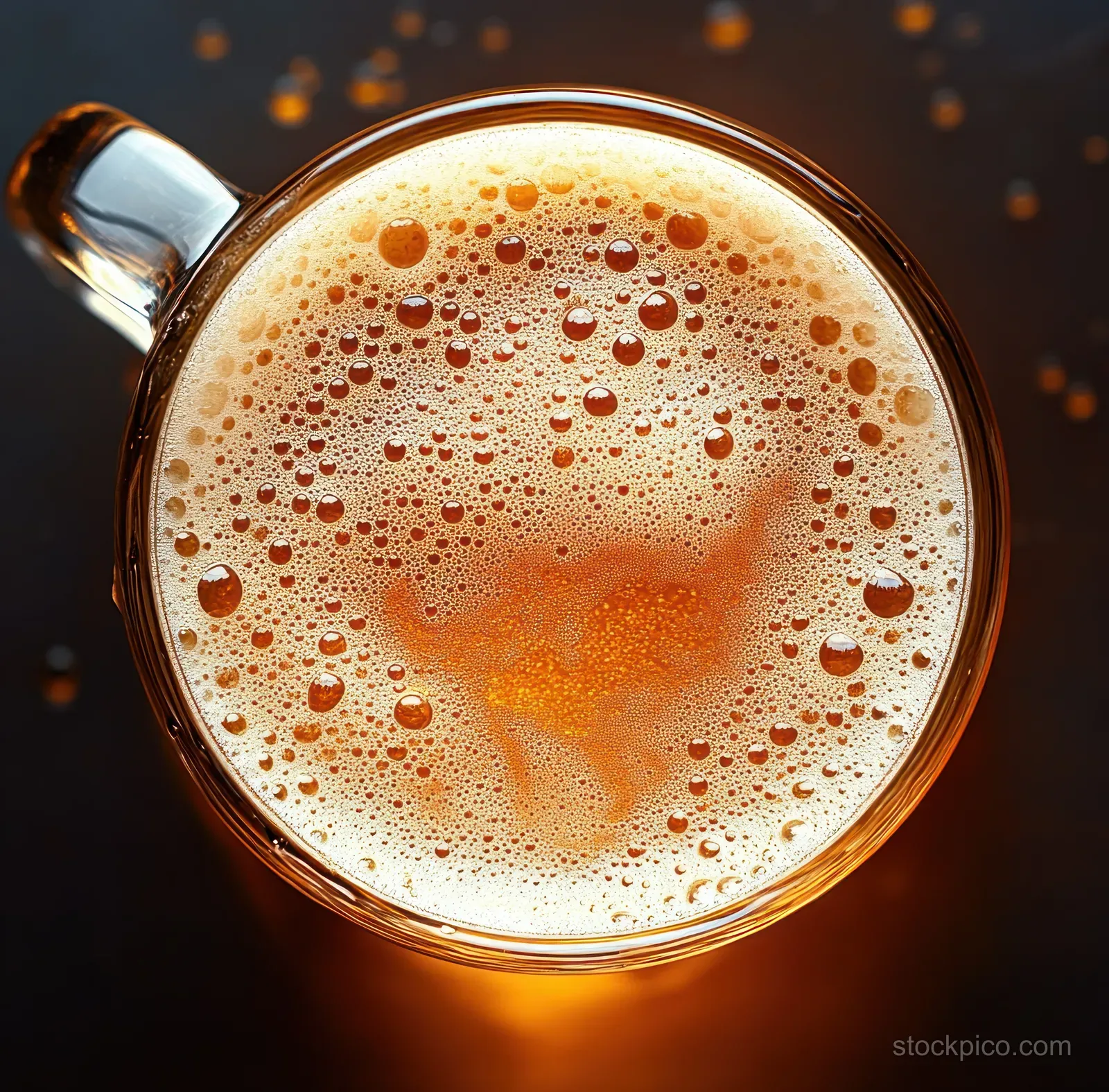 Top-down view of a transparent mug filled with frothy amber beer and visible bubbles on a dark background.