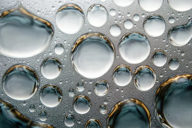 Mixed-size water droplets cling to a glass surface, reflecting light in an abstract circular arrangement.