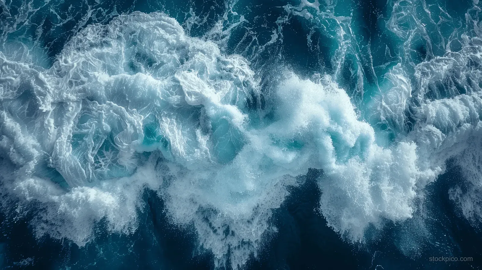 Top-down view of ocean waves breaking into white foam across dark turquoise water.