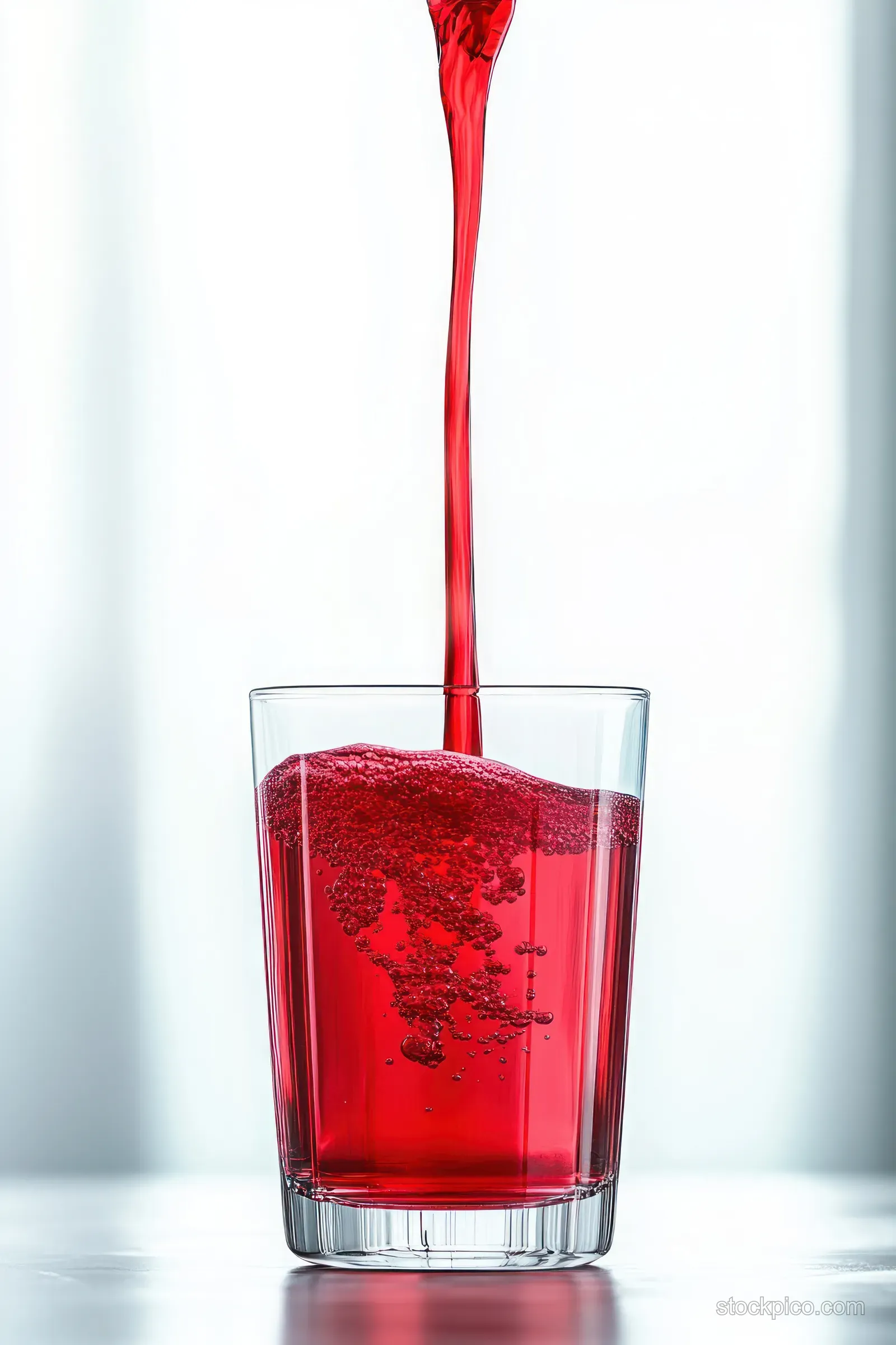 Red cherry juice stream pours into a clear glass, forming splashes and droplets on a white background.