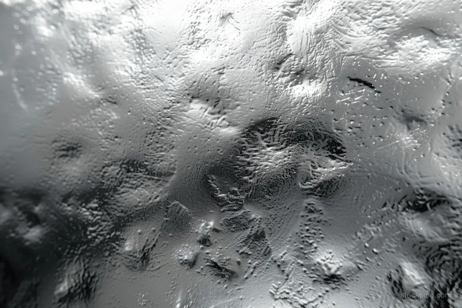 Textured silver-gray metal surface with scattered droplets and glossy reflections across the background.