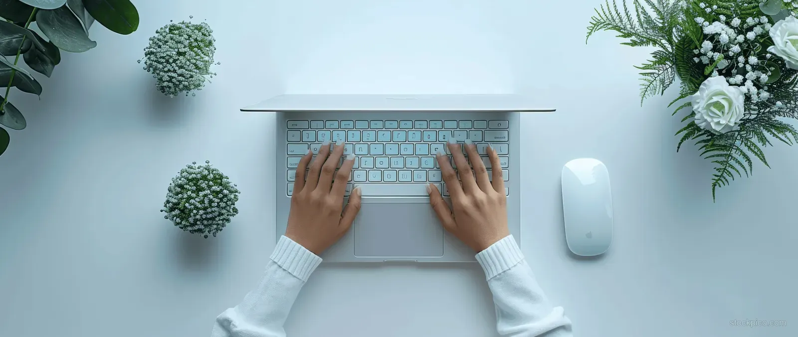 Close-up of hands typing on a laptop keyboard on a white desk in a clean office workspace.