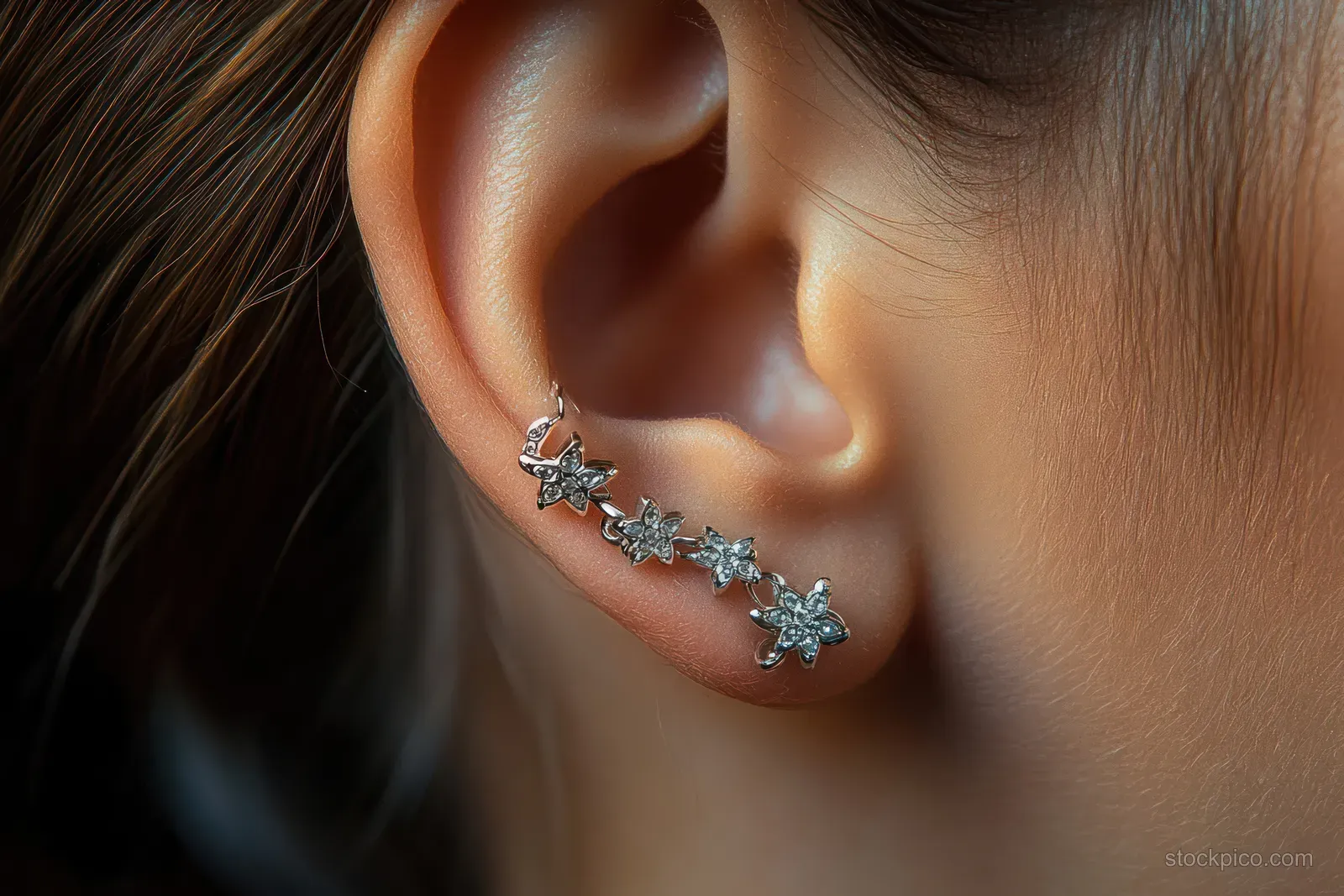Close-up of a female ear wearing a delicate silver floral chain earring with visible skin and hair strands.
