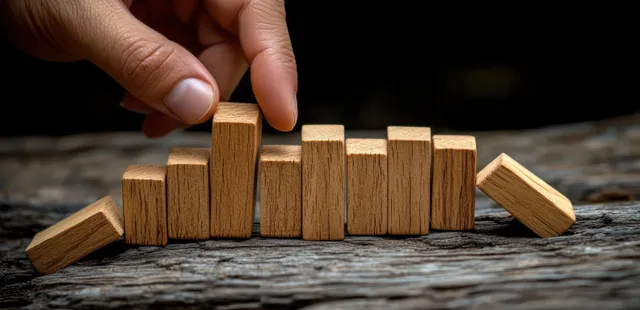 Hand stopping falling wooden dominoes on textured table during risk crisis management concept