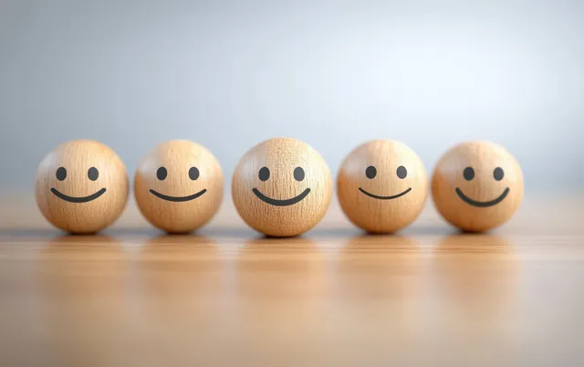 Smiling emoji-like faces arranged in a row on a wooden table, suggesting satisfaction ratings.