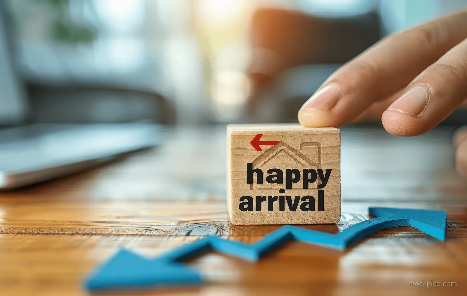 A hand moves a small sign with rising blue arrows on a wooden desk.
