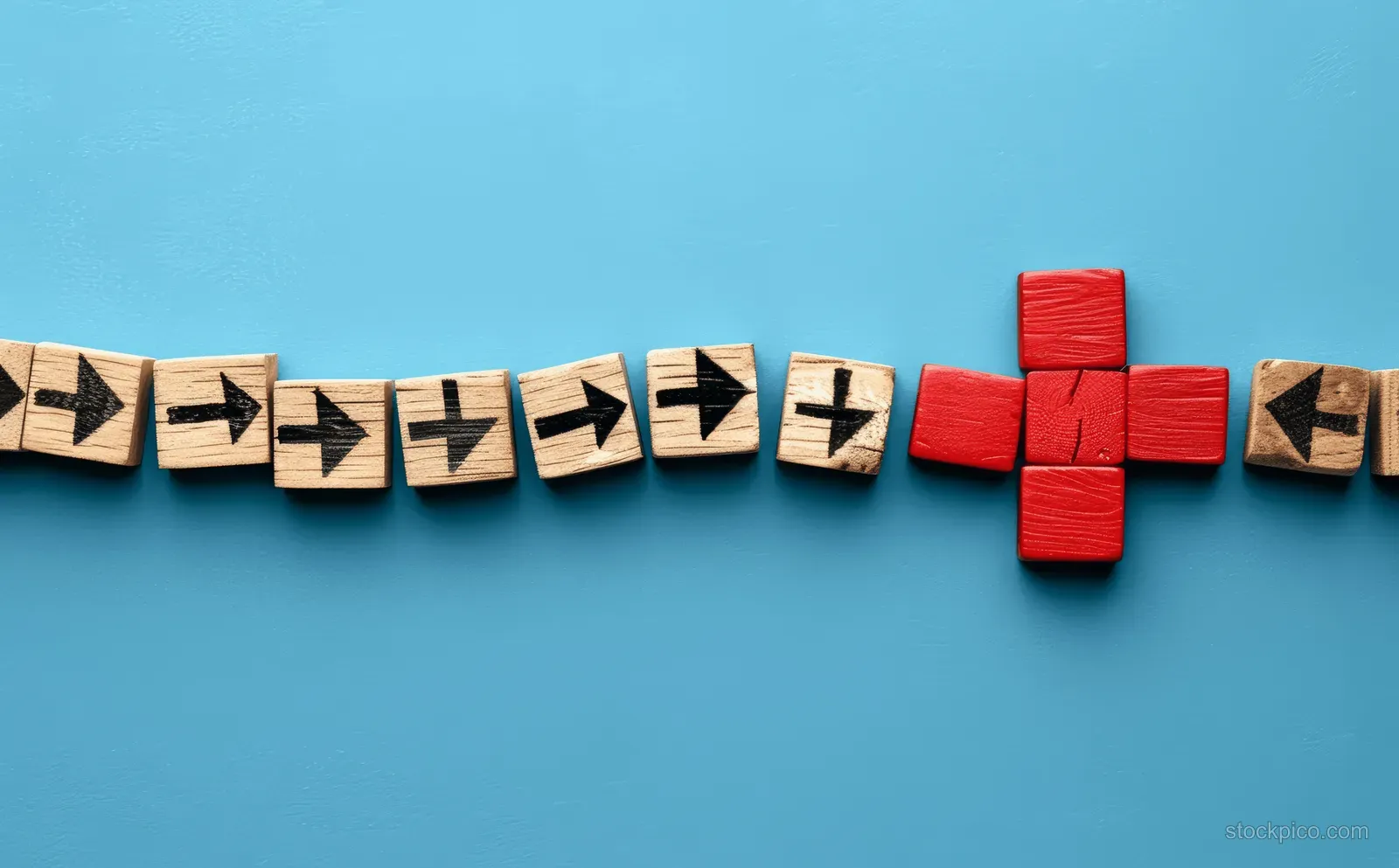 Red cross wooden block sits at the end of a curved arrow path made from black arrow wooden blocks on blue background.