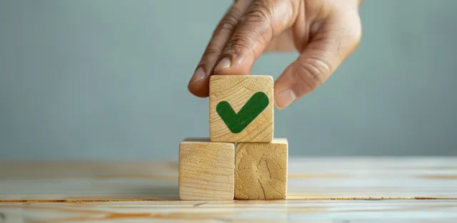 A hand places a wooden block marked with a green checkmark on a desk.