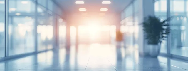 Blurred hospital corridor interior with light blue walls and panoramic window glow in soft bokeh.