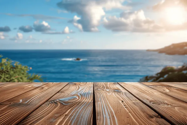 A wooden deck overlooks a tranquil ocean with clear blue water and soft clouds under warm sunlight.