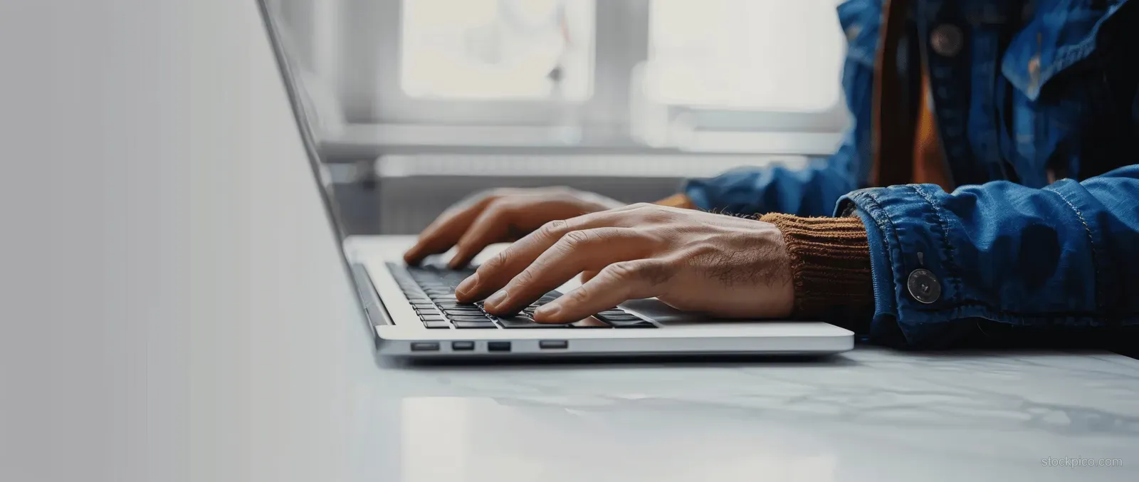 Hands typing on a laptop keyboard at an office desk, with a blurred background.