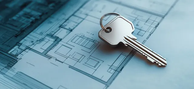 A metal house key fob lies on architectural blueprints with visible grid lines and measurement markings.