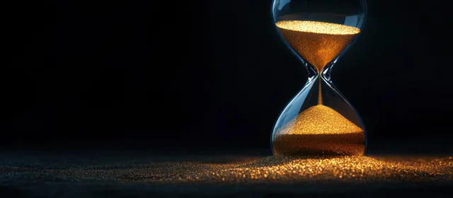 Golden sand flows through a transparent hourglass timer against a dark background, captured in close-up.