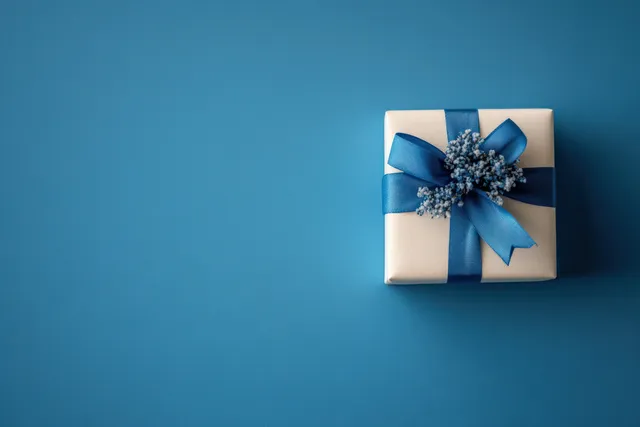 Gift box with blue ribbon and sparkly bow on deep blue minimalist background