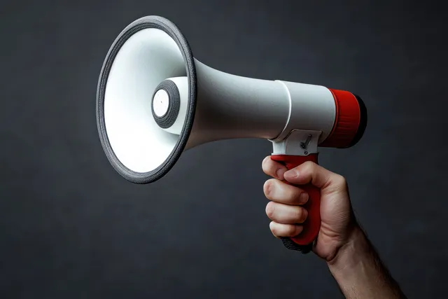 A hand firmly holds a white and red megaphone on a dark gray background.