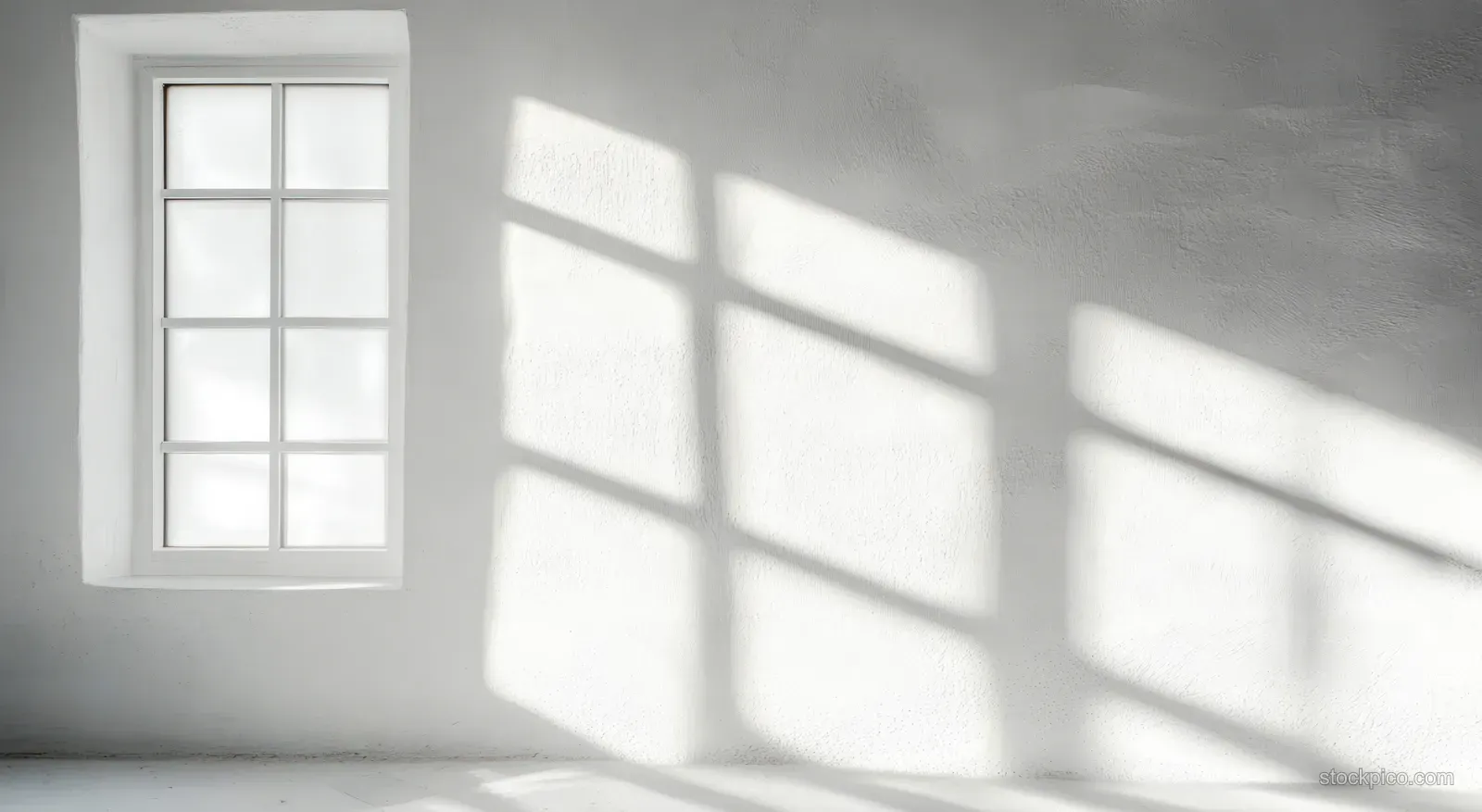 Daylight from a small grid window casts geometric shadows across a white interior wall and floor.