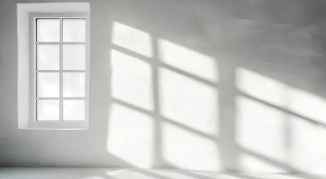 Daylight from a small grid window casts geometric shadows across a white interior wall and floor.