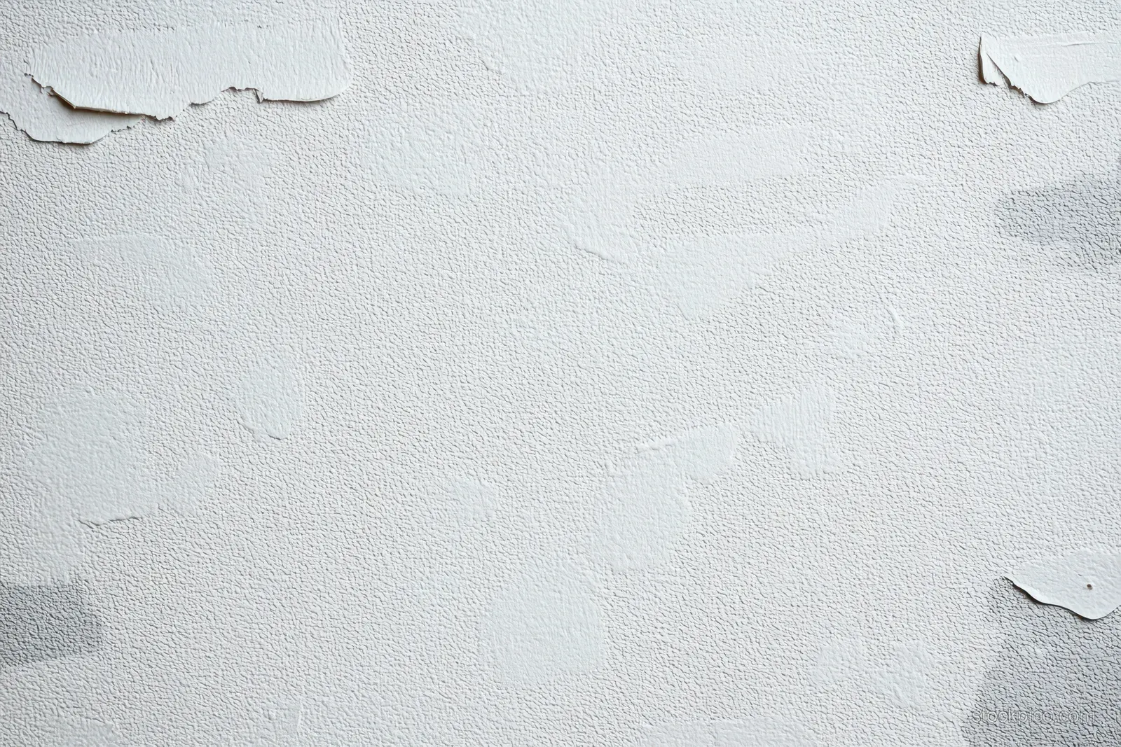 Close-up of a white wall with peeling paint, small cracks, and rough aged plaster texture.