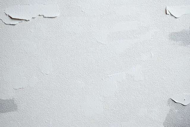 Close-up of a white wall with peeling paint, small cracks, and rough aged plaster texture.