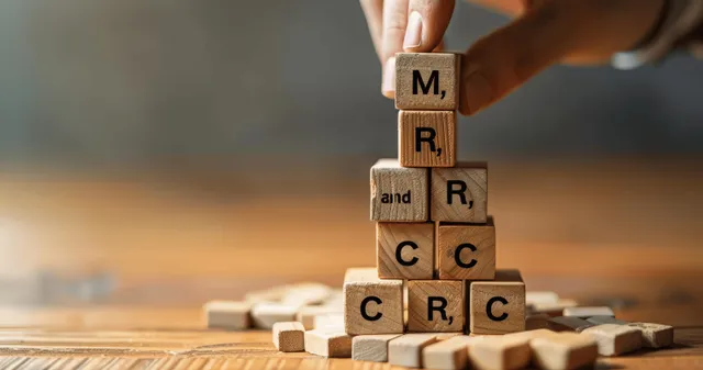 Hand stacks wooden letter blocks into a target-like structure with a blurred background.