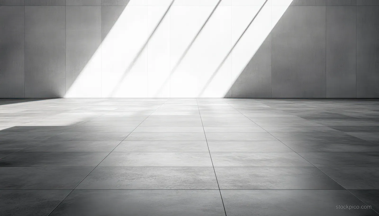 Empty interior room with large tiled floor and diagonal sunlight shadows on a plain wall.