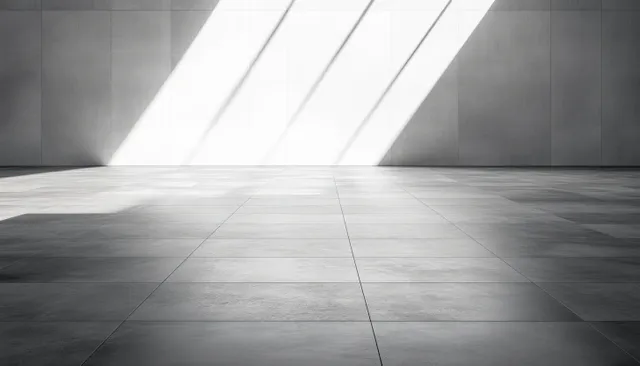 Empty interior room with large tiled floor and diagonal sunlight shadows on a plain wall.