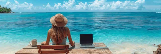 Woman in a straw hat working on a laptop on a beach deck with coffee, facing the turquoise ocean.