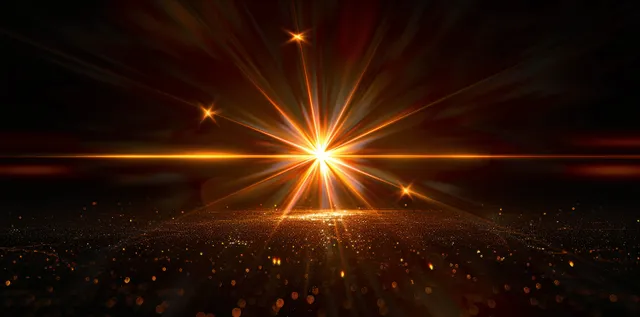 Golden starburst lens flare with warm rays on deep black background, glowing light beams
