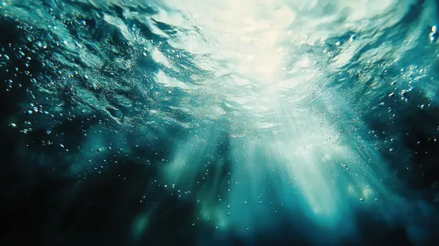 Sunlight rays shine through deep blue ocean water with scattered bubbles and moving ripples.