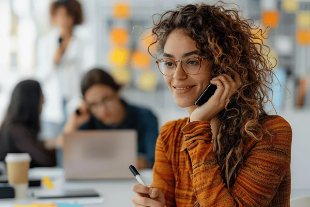 Curly-haired businesswoman smiling while talking on phone at office desk
