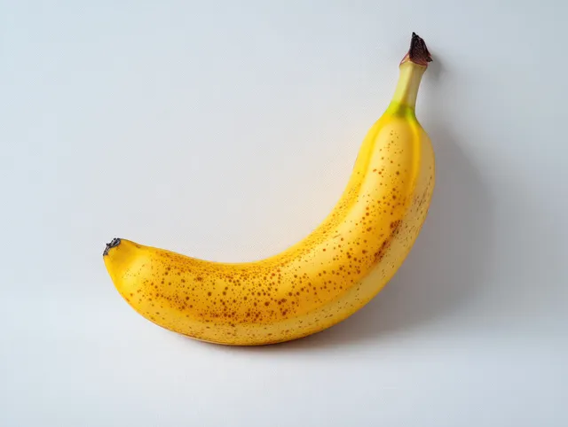 A single ripe yellow banana with brown speckles rests on a plain white background.