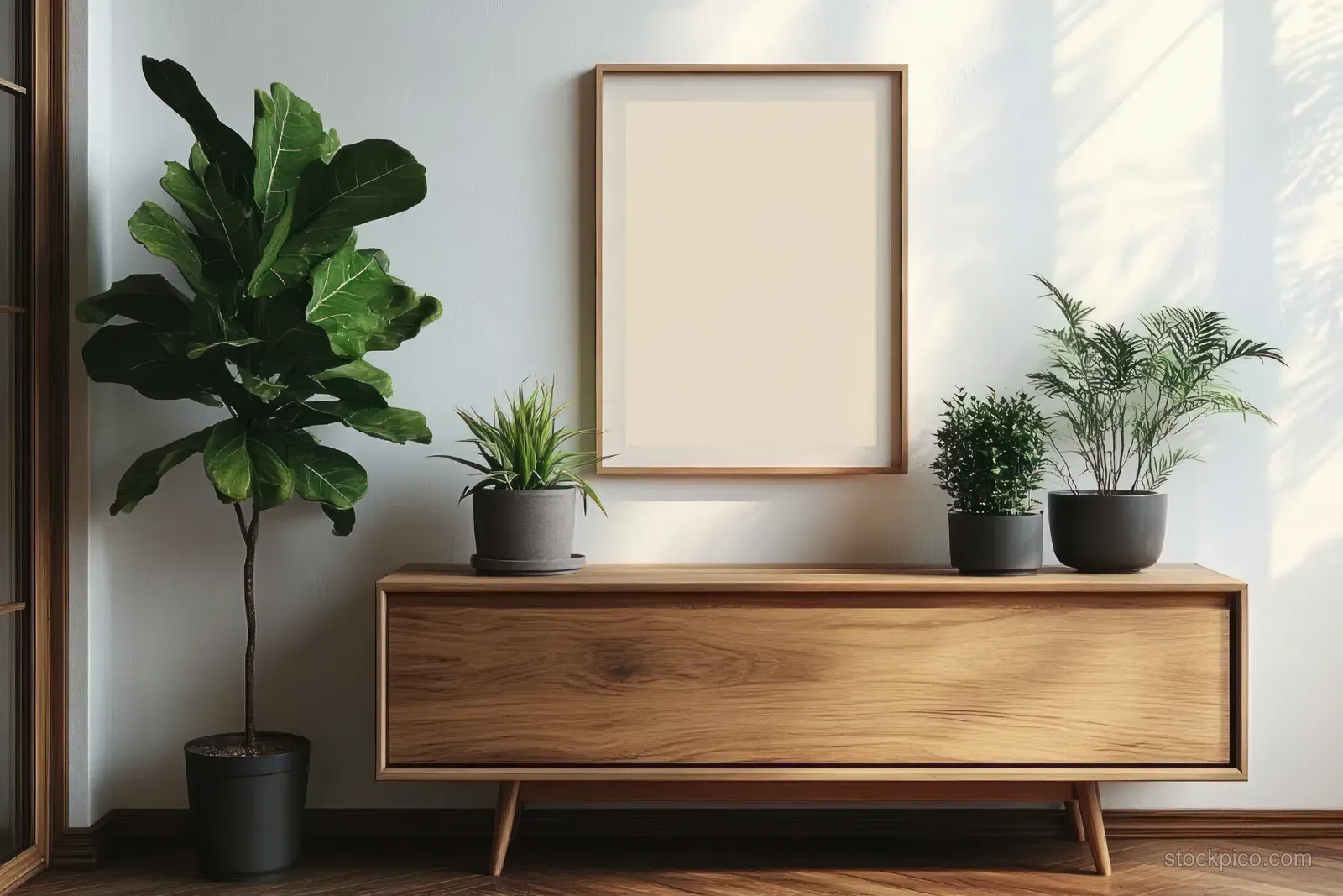 Minimal living room corner showing a wooden sideboard, three potted plants, and a framed print on a white wall.