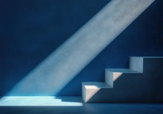Empty minimalist staircase lit by a soft beam, casting sharp shadows on a textured deep blue wall.