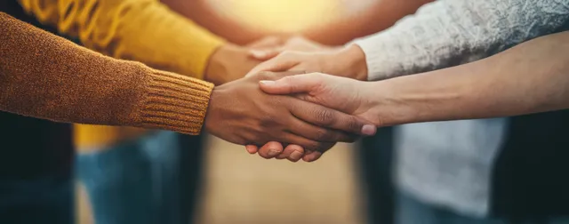 Diverse hands clasped together in teamwork gesture over a blurred office background