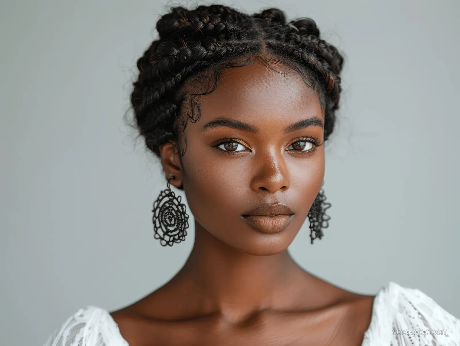 Close-up portrait of an African American woman with cornrow braids and ornate earrings.