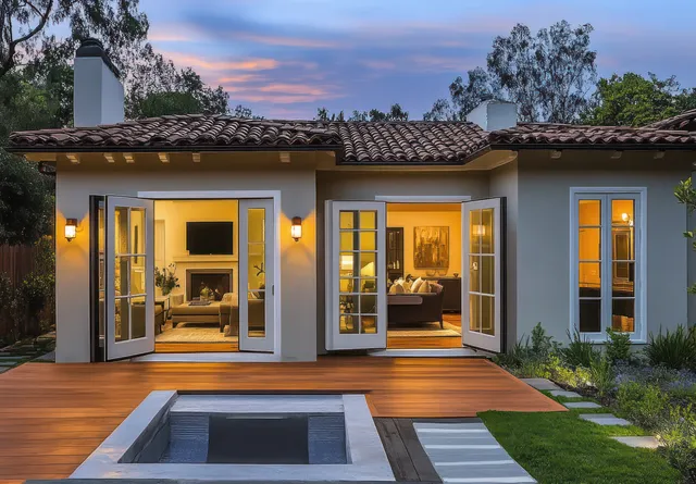 Single-story modern home at dusk with open French doors and a wooden deck