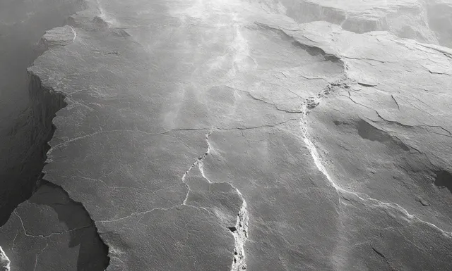 Cracked grey rock outcrop with deep fissures and uneven edges under soft diffused light